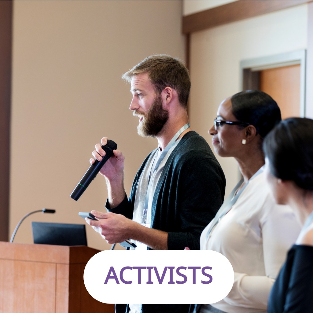 A man speaking into a microphone alongside panelists at a conference